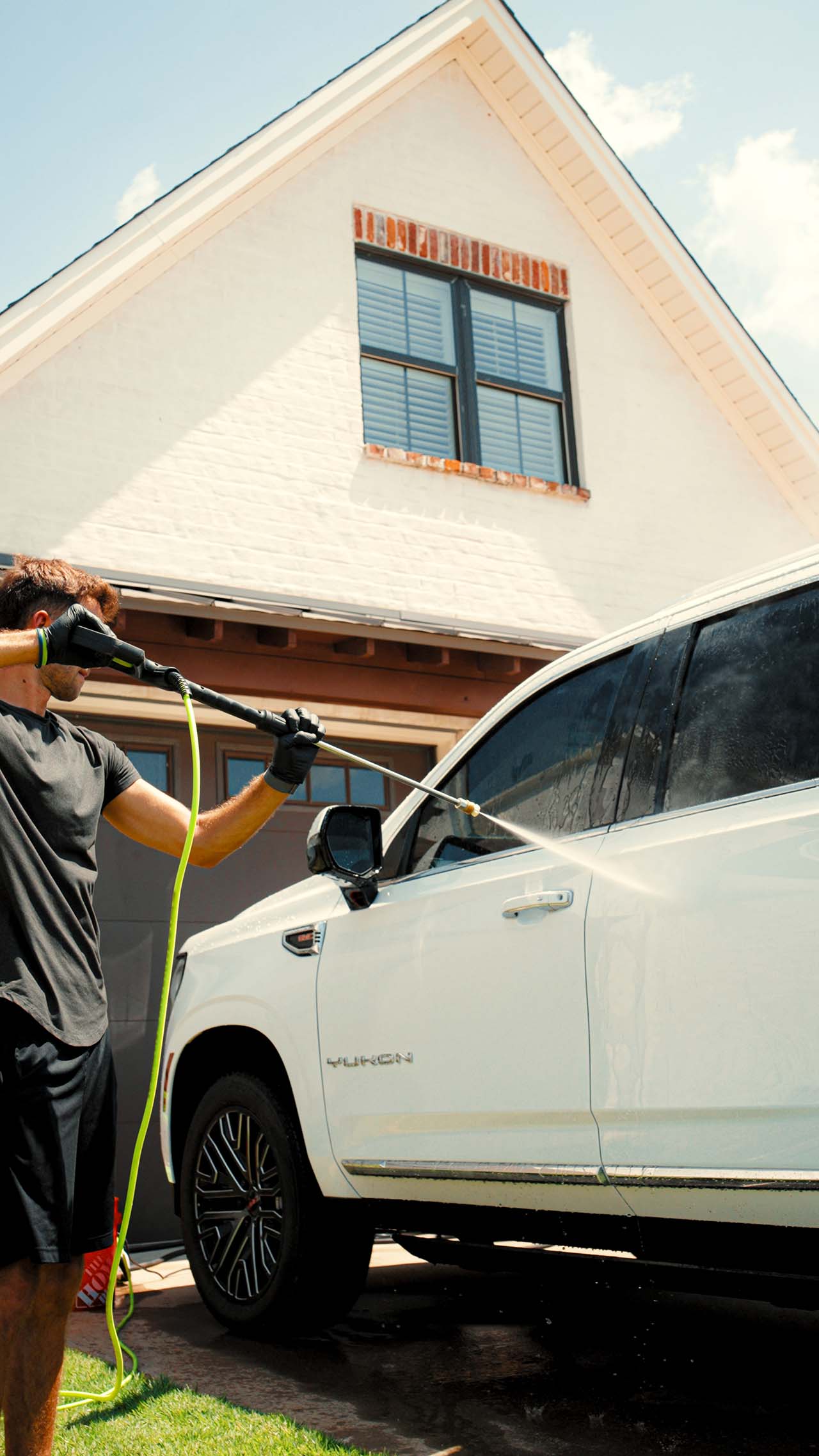 A detailer washing an SUV in the driveway at a home